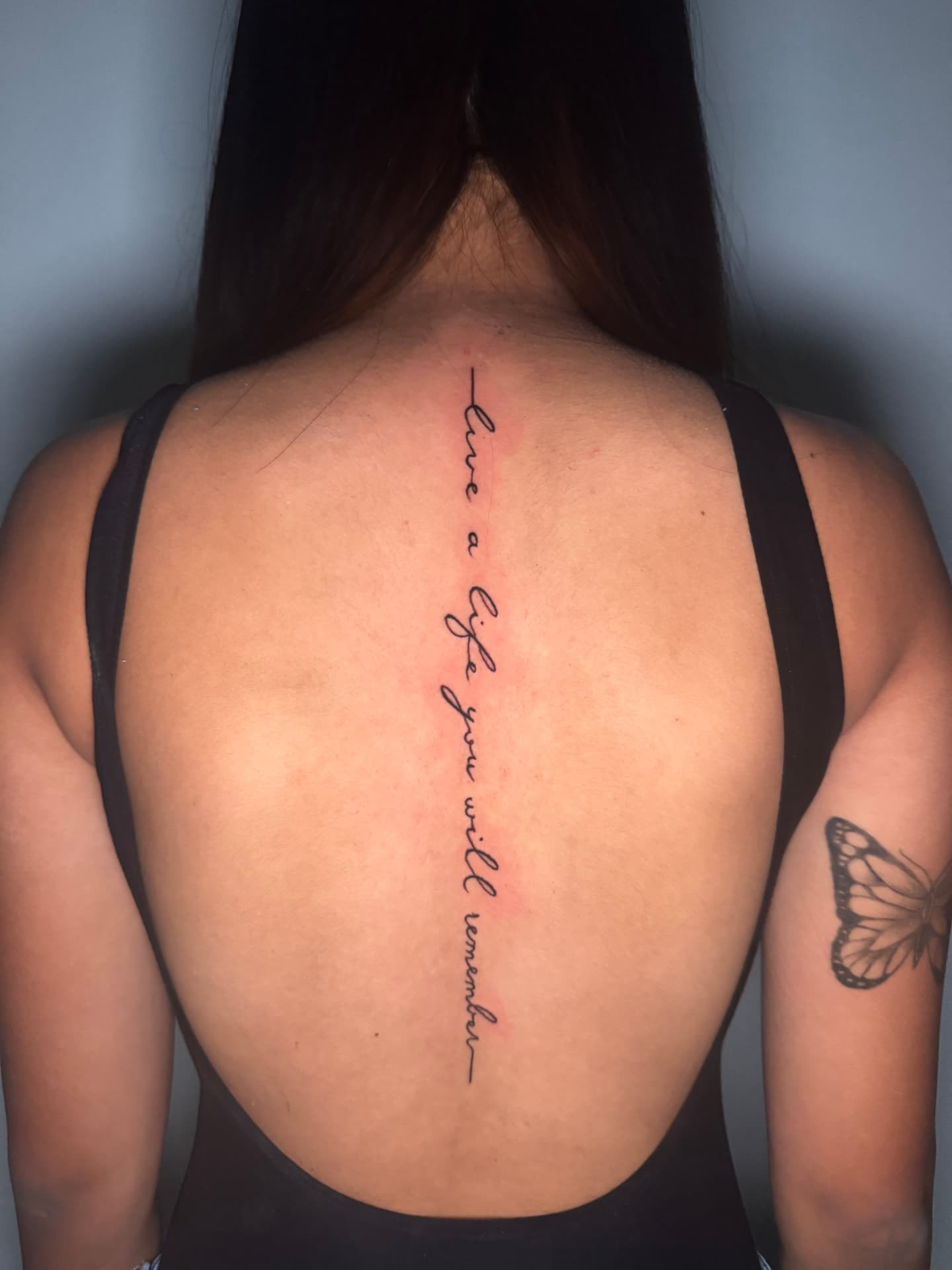 Fine-line script tattoo reading down the spine