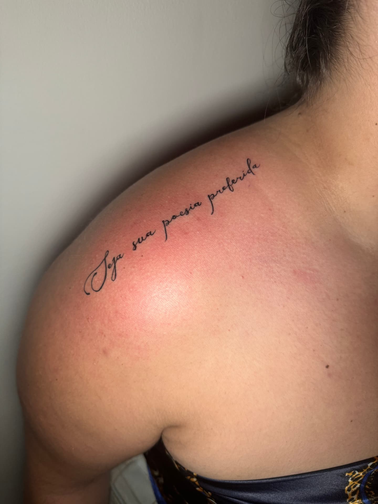 Fine-line cursive script tattoo across the shoulder