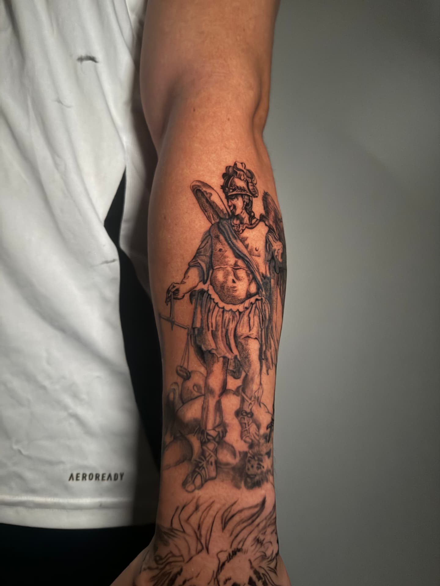 Black-and-grey St. Michael tattoo with scales on a forearm